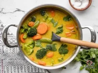 A bowl of creamy vegetable curry made with coconut milk and mixed vegetables, served with rice and fresh bread
