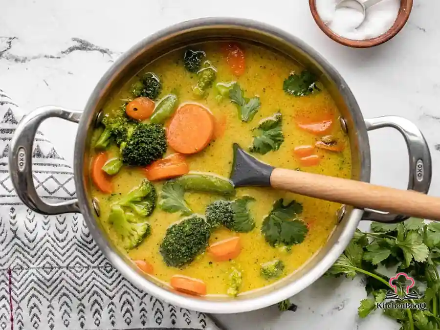 A bowl of creamy vegetable curry made with coconut milk and mixed vegetables, served with rice and fresh bread