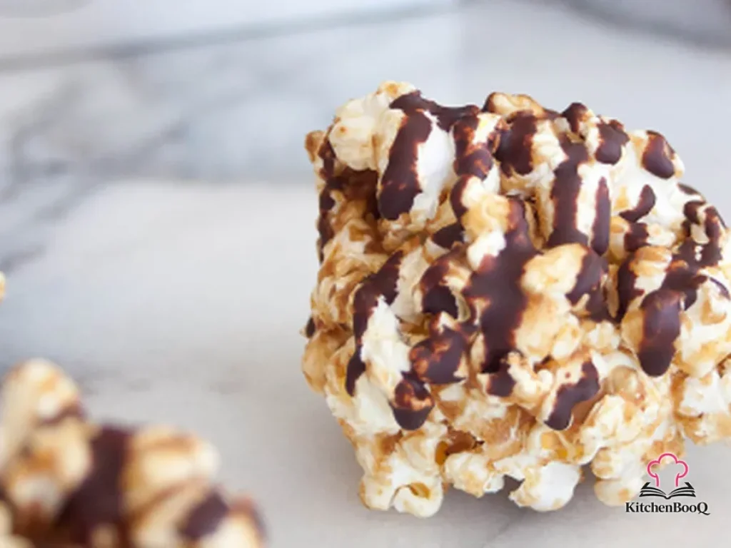 Two healthy popcorn balls drizzled with dark chocolate on a white plate, made with date caramel and sea salt popcorn