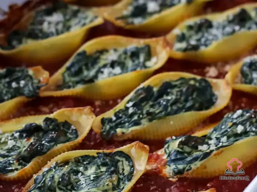 Baked jumbo pasta shells stuffed with spinach and ricotta cheese in marinara sauce, topped with grated hard cheese in a rectangular baking dish