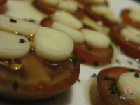 Sliced fresh tomatoes topped with thin rounds of string cheese, drizzled with basil-infused olive oil and sprinkled with Hawaiian black lava salt on a white serving plate