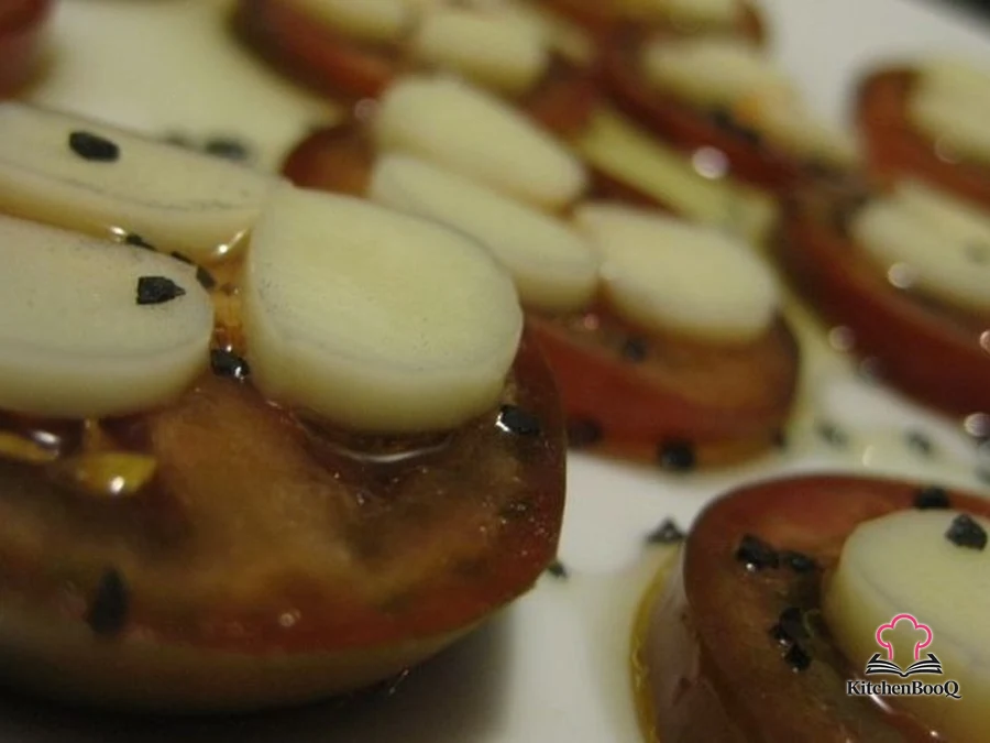 Sliced fresh tomatoes topped with thin rounds of string cheese, drizzled with basil-infused olive oil and sprinkled with Hawaiian black lava salt on a white serving plate