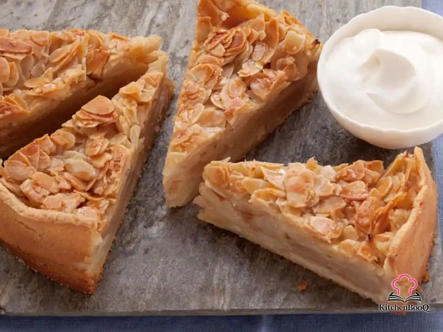 A golden double-crust Almond Apple Pie with steam vents on top, set on a rustic wooden surface with sliced apples and cinnamon sticks nearby