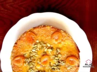 Gluten-free almond apricot cardamom cake topped with whole poached apricots and pumpkin seeds on a white cake stand