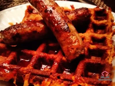 Crispy almond flour sweet potato waffles stacked on a white plate drizzled with agave sriracha sauce and garnished with fresh herbs