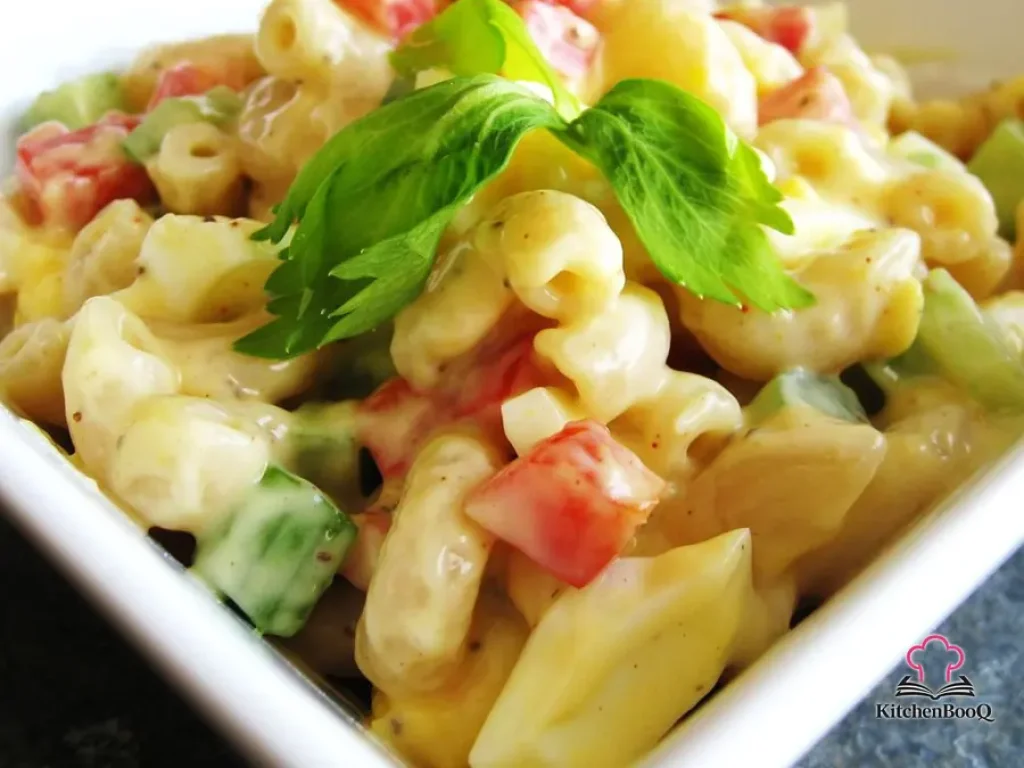 Bowl of Amish macaroni salad with elbow pasta, hard-boiled eggs, red bell pepper, and celery in a creamy yellow dressing