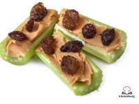Celery stalks filled with creamy peanut butter and topped with plump raisins arranged on a white plate