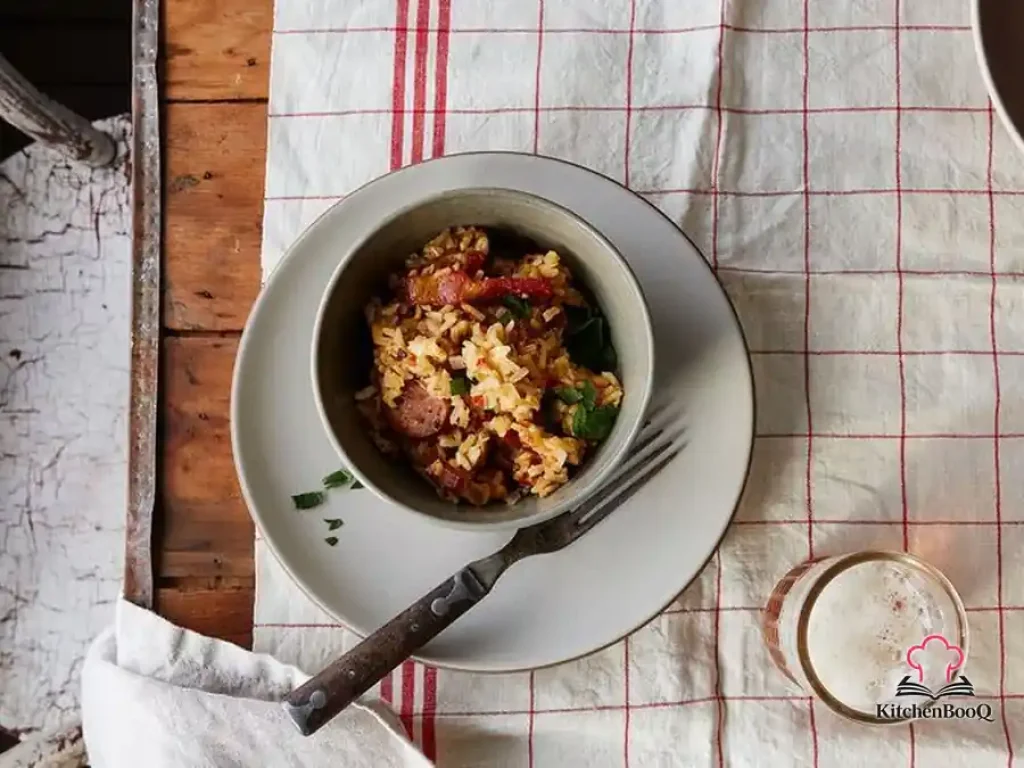 A large Dutch oven filled with Anytime Jambalaya showing sliced andouille sausage, scrambled eggs, bacon pieces, and fluffy Cajun-seasoned rice garnished with fresh minced parsley