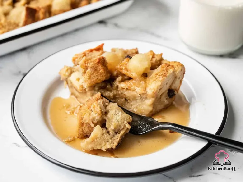 Golden baked apple cinnamon bread pudding in a white casserole dish topped with dollops of applesauce and a dusting of cinnamon