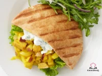 Open pita bread filled with curry-spiced turkey chunks, thin apple slices, and sautéed onions, drizzled with plain yogurt on a wooden board