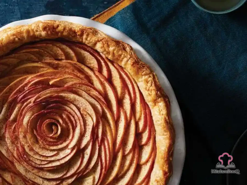 Overhead view of a sliced apple rose pie with petal-like apple spirals arranged on a creamy filling in a golden almond shortcrust