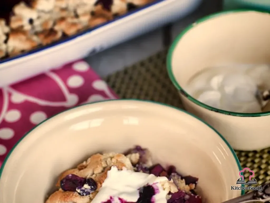 Warm apple and blueberry crumble in a square baking tin topped with golden almond flour crumble and drizzled with honey-fruit syrup