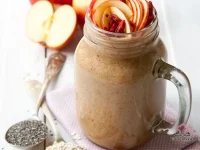 A tall glass of creamy apple and oat smoothie topped with a sprinkle of cinnamon and oats, served with a fresh apple and banana in the background