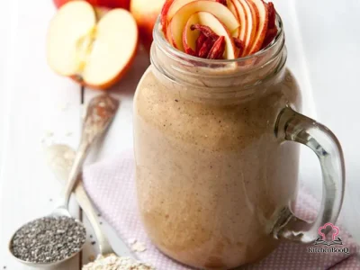 A tall glass of creamy apple and oat smoothie topped with a sprinkle of cinnamon and oats, served with a fresh apple and banana in the background