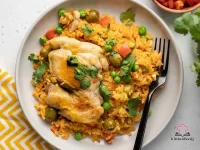 A Dutch oven filled with golden Puerto Rican arroz con pollo, featuring seared chicken thighs resting on saffron-colored rice dotted with green peas, red bell pepper, and olives, garnished with fresh cilantro