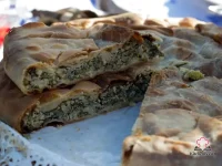 Golden baked Ligurian Torta Verde sliced to reveal layers of ricotta, artichoke and chard filling in a flaky olive oil crust, served on a rustic wooden board