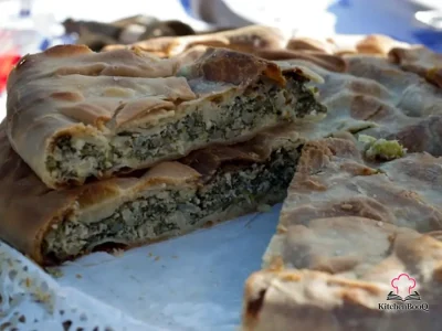 Golden baked Ligurian Torta Verde sliced to reveal layers of ricotta, artichoke and chard filling in a flaky olive oil crust, served on a rustic wooden board