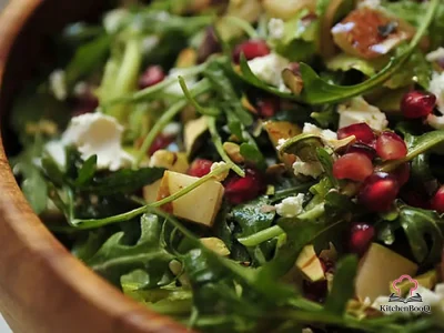 Arugula pear and goat cheese salad topped with pomegranate seeds and pistachios in a large serving bowl with pomegranate vinaigrette