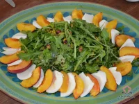 Arugula salad topped with roasted peach quarters, fresh mozzarella slices, and pistachios on a white serving platter drizzled with balsamic vinaigrette