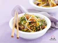 Asian beef noodle salad in a large bowl with sliced rump steak, Singapore noodles, beansprouts, grated carrot and green onions dressed in sesame ginger soy marinade