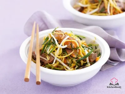 Asian beef noodle salad in a large bowl with sliced rump steak, Singapore noodles, beansprouts, grated carrot and green onions dressed in sesame ginger soy marinade