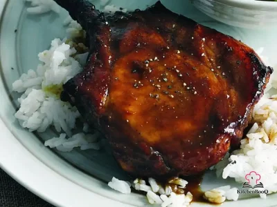 Asian-glazed pork cutlets drizzled with char siu honey sauce on a plate with orange and avocado salad and steamed white rice