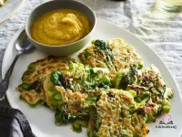 Stack of golden asparagus and leek pancakes on a white plate drizzled with creamy apple-miso mayo and garnished with fresh watercress