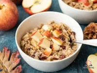 A bowl of creamy autumn oatmeal topped with sautéed cinnamon apple pieces, dried cranberries, chopped walnuts, and a drizzle of maple syrup on a rustic wooden table