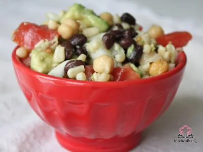 A large bowl of avocado bean salad with cubed avocado, black beans, chickpeas, corn, diced tomatoes and onion, garnished with fresh herbs