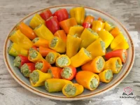 Colorful mini sweet peppers stuffed with creamy avocado pesto filling arranged on a white serving platter