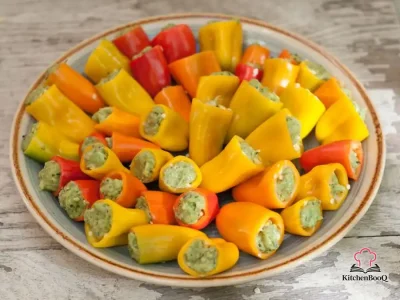 Colorful mini sweet peppers stuffed with creamy avocado pesto filling arranged on a white serving platter
