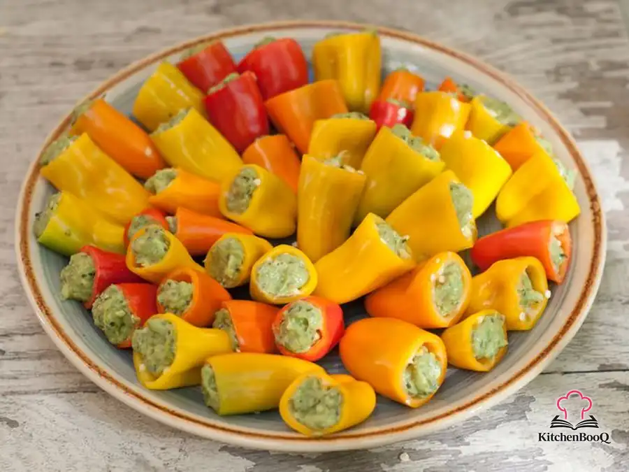 Colorful mini sweet peppers stuffed with creamy avocado pesto filling arranged on a white serving platter