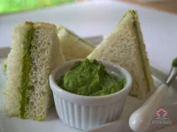 Crustless avocado and cucumber finger sandwiches cut into rectangles, stacked on a white plate with fresh mint leaves and lime wedges on the side