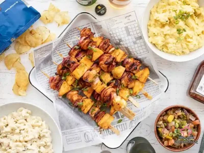 Grilled BBQ chicken kebabs with pineapple chunks and red onion on skewers, glazed with smoky BBQ sauce and topped with sliced green onions on a wooden serving board