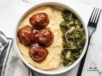 Bowl of creamy cheddar cheese grits topped with four glazed BBQ pork meatballs and a drizzle of smoky BBQ sauce