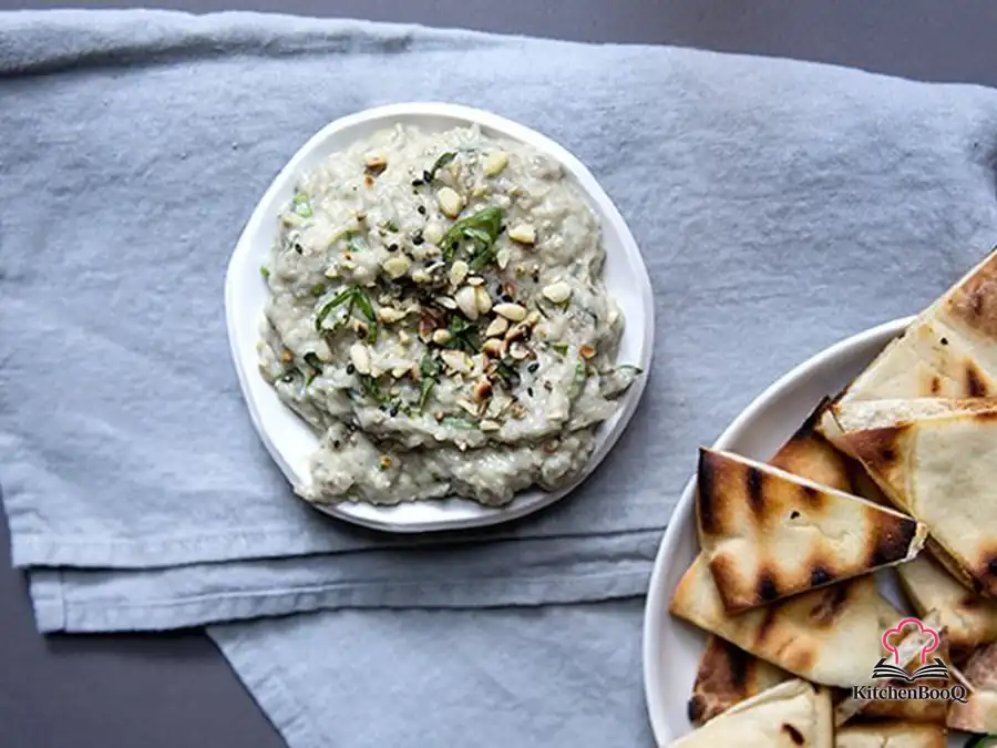 Creamy baba ganoush in a rustic bowl garnished with fresh parsley, basil, toasted pine nuts, sesame seeds, and a drizzle of olive oil
