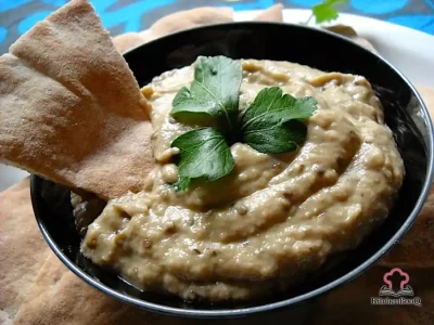 A bowl of creamy baba ganoush topped with paprika and olive oil, served with warm pita triangles and fresh vegetable crudités on a rustic wooden board