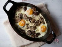 Baked eggs with sautéed mushrooms and melted Gruyere cheese in a white baking dish, served warm