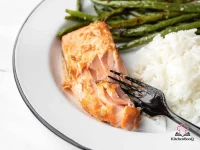 Four glazed baked ginger salmon fillets on a parchment-lined baking sheet with a caramelized golden-brown crust