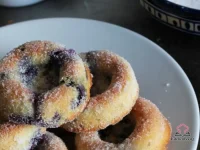 Golden baked wholemeal blueberry donuts on a white serving plate, dusted with sugar and studded with fresh blueberries