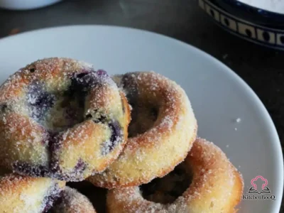 Golden baked wholemeal blueberry donuts on a white serving plate, dusted with sugar and studded with fresh blueberries