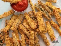 Golden crispy baked zucchini fries coated in panko and Parmesan arranged on a wire rack with a small bowl of pizza sauce for dipping