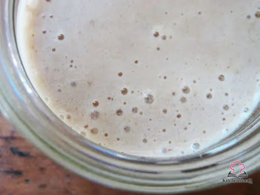 A tall glass of thick banana chai ginger smoothie topped with a sprinkle of cinnamon and a slice of fresh ginger on the rim