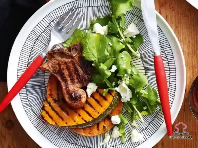 Barbecued spiced lamb loin chops served alongside chargrilled pumpkin wedges and a fresh rocket salad topped with crumbled goat's cheese on a large platter