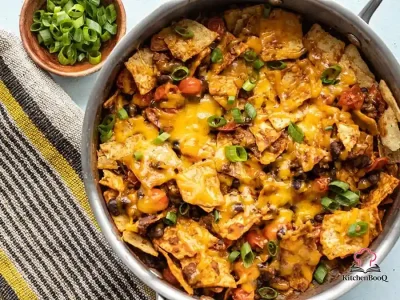 Beef taco skillet with seasoned ground beef, black beans, grape tomatoes, tortilla chips, melted cheddar cheese, and sliced green onions in a cast iron skillet