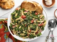 Large bowl of kale pasta salad with penne, chickpeas, halved grape tomatoes, red onion, and grated Parmesan tossed in a creamy balsamic vinaigrette