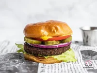 A golden-brown black bean burger patty served in a toasted bun with fresh toppings on a wooden board