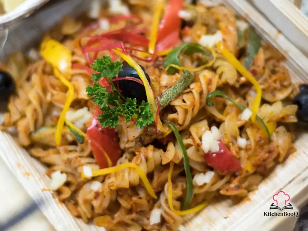 A bowl of pasta tossed with flaked salmon, black olives, and sun-dried tomatoes in a glossy white wine sauce, garnished with fresh Italian herbs