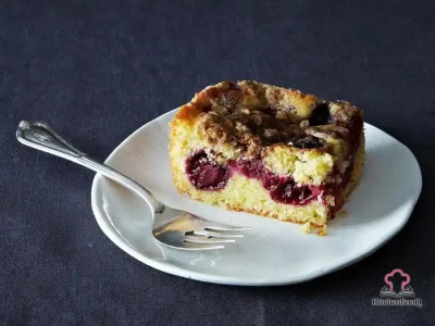 Slice of blackberry cornbread buckle with oatmeal crumb topping and juicy berry filling on a white plate