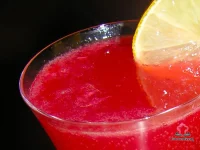 A Prosecco flute filled with deep ruby Bloody Ginger cocktail garnished with a Meyer lemon slice on a white marble surface